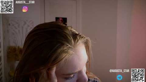 Media: Video of a woman with light brown hair, looking down, in a dimly lit room with a white wall and a QR code overlay.