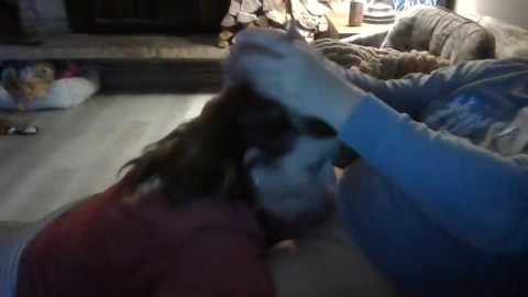 Media: Video of a person with long brown hair, wearing a red sweater, being comforted by another person with a blue shirt, in a dimly lit living room.