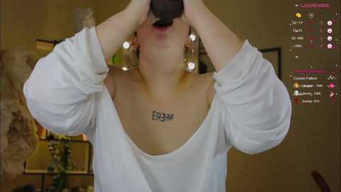 Media: A video shows a light-skinned woman with a tattoo of \"Esgaroth\" on her collarbone, wearing a white off-shoulder sweater, holding a camera, indoors with a cozy atmosphere and a social media overlay.