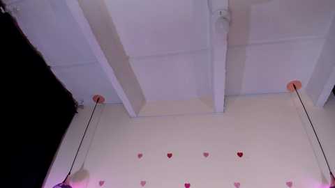 Media: A video of a white ceiling with exposed wooden beams and a black curtain partially visible on the left. Red heart-shaped stickers are evenly spaced on the ceiling, adding a playful touch.