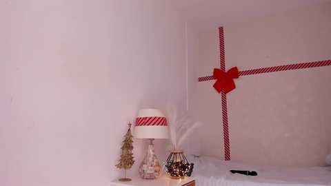 Media: Video of a minimalist Christmas corner featuring a white lamp with red stripe, a red gift bow, a small tree, and a candle in a glass jar on a snow-covered surface.