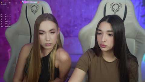 Media: Video of two young women with fair skin, long straight hair, and pouty lips, wearing sleeveless tops. They sit on gaming chairs against a purple background, with chat windows visible.