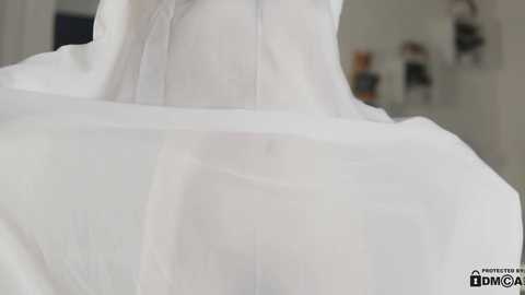 Media: Video of a white wedding dress with delicate lace sleeves and a flowing train, captured from behind. The background is softly blurred, featuring a modern, minimalist bridal salon with neutral tones.