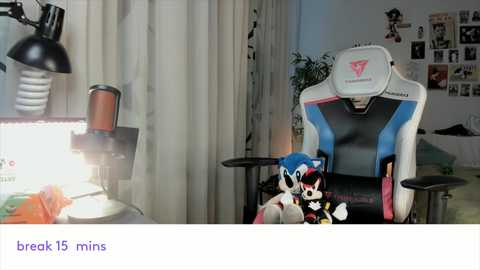 Media: A video of a gamer's setup: a blue and black gaming chair with a mouse pad, a plush Sonic the Hedgehog toy, a desk lamp, and a green plant in the background.