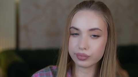 Media: A video of a young woman with light skin, straight blonde hair, and light makeup, wearing a plaid shirt, making a pouty face. Background is out of focus.