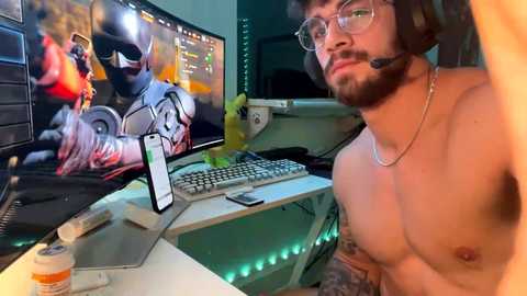 Media: Video of a shirtless, tattooed man with glasses, wearing headphones, in a dimly-lit gaming room with multiple screens, including one showing a violent video game scene.