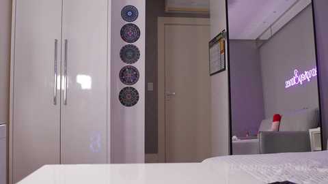 Media: A video of a modern bedroom with white furniture, a mirrored closet, and purple accents; a framed photo and decorative plates adorn the walls.