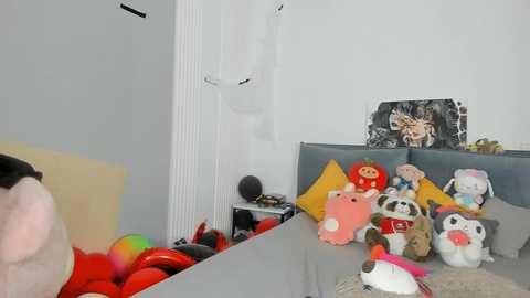 Media: Video of a cluttered bedroom with a messy bed covered in colorful stuffed animals, including a panda and a red bear, against a white wall featuring a framed black-and-white photo.