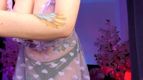 Media: A video of a partially visible woman in sheer, polka-dot lingerie with a colorful peacock feather tattoo on her arm, standing in a dimly lit room with a Christmas tree and glowing red lights in the background.