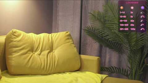 Media: Video of a modern living room featuring a mustard-yellow sofa with a tufted cushion, a potted fern, and a digital clock displaying various times.