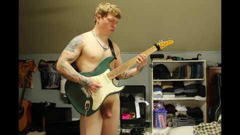 Media: Video of a shirtless, tattooed man with short blonde hair, holding a green electric guitar in a cluttered room with beige walls, bookshelves, and musical instruments.