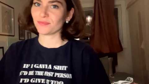 Media: A video of a young woman with shoulder-length brown hair, fair skin, and blue eyes, wearing a black t-shirt with white text reading, \"IF I GAVE A SHIT, I'D BE THE FIRST PERSON TO.\