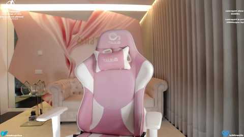 Media: Video of a pink gaming chair with a white headrest, in a modern, cozy living room with beige curtains and a cream sofa, illuminated by soft, ambient lighting.