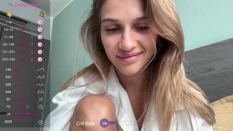 Media: Video of a smiling young woman with long blonde hair, wearing a white blouse, in a bedroom with teal walls. Live stream overlay shows heart and like counts.