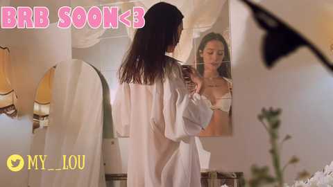 Media: A video of a woman in a white robe, holding a phone, looking in a mirror. Text overlay reads \"BBB SOKK MY LOU.\