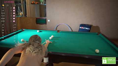 Media: A video of a nude woman with long blonde hair, leaning over a green pool table, playing pool in a dimly lit room with a \"Mystery\" sign on the wall.