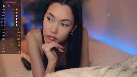 Media: Video of an Asian woman with long black hair, lying on a bed, looking contemplative. She has a slender build, wearing minimal makeup, and is topless. Background is blurred with soft lighting.