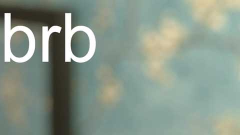 Media: A video of a blurred, teal and beige wall with a partially visible, dark window frame on the left side. The word \"brrb\" is prominently displayed in large, white, sans-serif font on the left. The image has a soft, out-of-focus aesthetic.