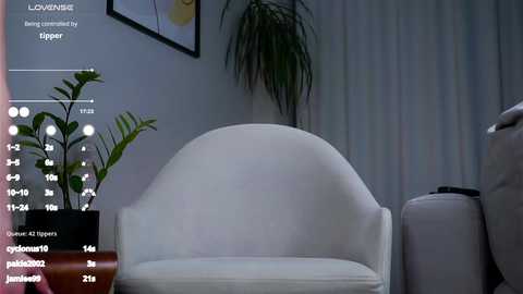 Media: Video of a modern, white armchair in a minimalist room with a potted fern, framed artwork, and light gray curtains. Digital overlay showing \"LOVEHACK\" and \"Tigger\" information.