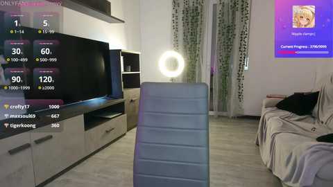 Media: Video of a modern, well-lit living room with a flat-screen TV, a glowing ring light on a tripod, a sofa, and a bright, colorful poster on the wall.