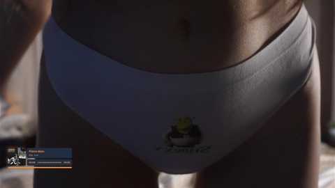 Media: A video of a woman's lower torso, wearing white underwear with a yellow and black logo, and a small tattoo on her right thigh. The background is blurred.