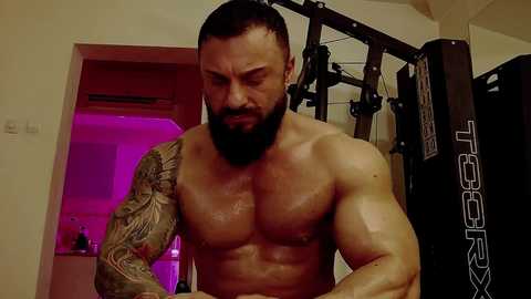 Media: Video of a shirtless, muscular, bearded man with a tattooed arm, working out in a dimly lit gym.