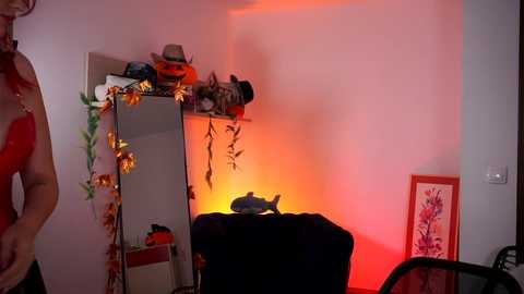 Media: Video of a dimly lit room with a woman in a red bra, a black cat, a jack-o'-lantern, and Halloween decorations, illuminated by a warm orange glow.