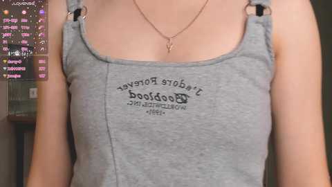 Media: Video of a woman wearing a gray tank top with a \"Tulsa Boxx\" logo and heart necklace, in a blurred indoor setting.