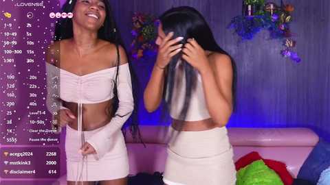 Media: Video of two young Black women in matching white off-shoulder mini dresses, laughing, with a social media feed in the background.