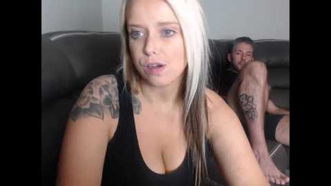 Media: A video of a blonde woman with tattoos and a black tank top, sitting on a couch with a shirtless man in the background.