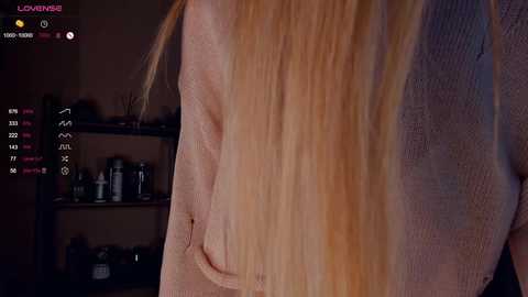 Media: Video of a close-up of a woman's back, showing her long, straight blonde hair and a visible scar on her shoulder. Background features a dimly lit room with a shelf containing various objects.