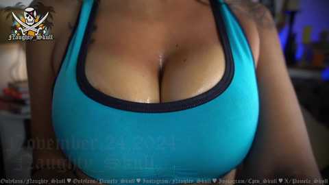 Media: A video of a woman with tan skin and large, round breasts wearing a turquoise sports bra, with a tattoo on her left shoulder. Background includes blurred objects and a watermark.