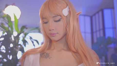 Media: Video of an Asian woman with long, pastel pink hair in cosplay attire, featuring pointed ears and a bandage on her neck. Background includes a green plant and a softly lit room.