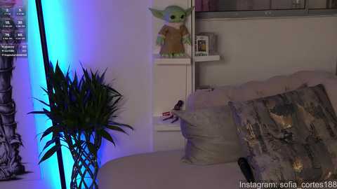 Media: Video of a cozy living room featuring a plush sofa, decorative pillows, a potted plant, a toy droid, and a framed picture, with a blue ambient light illuminating the scene.