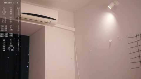 Media: Video of a minimalist, beige-tiled bathroom with an air conditioner above a white door, a metal towel rack on the right, and a digital clock displaying a time of 11:43.