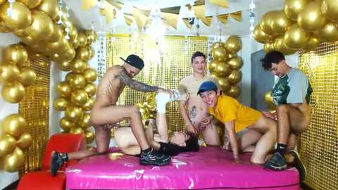 Media: Video of a raucous party with five shirtless, tattooed men in gold balloons, one wearing a yellow cap, in a room decorated with gold and white streamers.