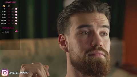 Media: Video of a bearded man with short, dark hair and a serious expression, in a dimly lit room. Social media icons and watermark in the bottom left corner.