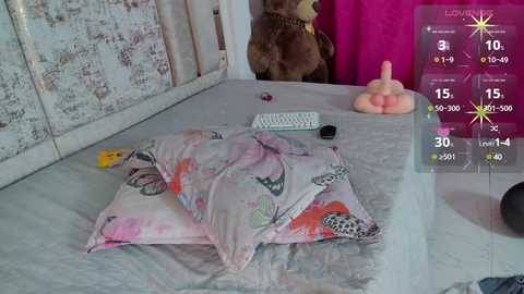 Media: Video of a messy bedroom with a bear toy, a white keyboard, a pink dildo, and a bed covered with colorful pillows.