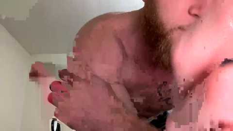 Media: Video of a nude, muscular man with a beard, holding a cellphone, standing indoors with blurred background.