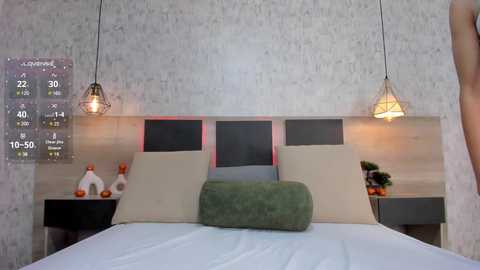 Media: A video of a modern bedroom with a beige and grey headboard, two pendant lights, a green cushion, and a digital clock on the wall.