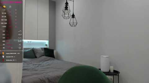 Media: Video of a modern bedroom with a grey bed, white wall, and two black industrial-style pendant lights. The bed features grey bedding and a green chair is partially visible in the foreground.