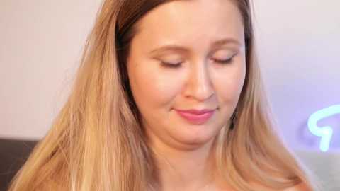 Media: Video of a young Caucasian woman with long, straight, blonde hair, wearing a black headband, smiling gently, in a softly lit indoor setting.