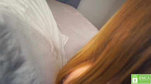 Media: Video of a close-up view of a person lying in bed, with a wooden headboard and light gray bedding. The person's long, light brown hair is partially visible.