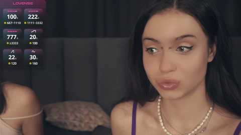 Media: Video of a young woman with long black hair, light skin, and a slender physique, wearing a purple top and pearl necklace, making a pouty face.