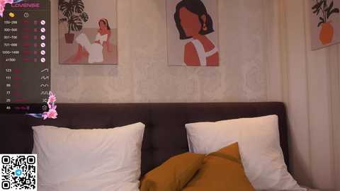 Media: Video of a modern bedroom with a dark brown headboard, two white pillows, and a mustard-yellow throw. The wall features two large, abstract paintings. A QR code and website link are visible in the bottom left corner.