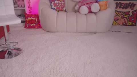 Media: Video of a plush, white, inflatable sofa with cartoon characters, on a light pink carpet. The background features vibrant, colorful artwork and a red stool. The setting exudes a playful, cartoon-themed atmosphere.