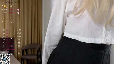 Media: A video shows a person from behind in a white blouse and black skirt, standing near beige curtains and a wooden chair. A QR code is visible in the bottom left corner.