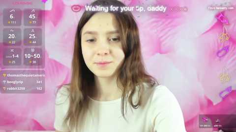 Media: Video of a young woman with long brown hair, fair skin, and a soft smile, wearing a white top. Background features a pink floral pattern with a \"Waiting for your tip, daddy\" text.