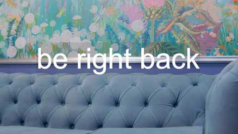 Media: A video of a light blue, tufted velvet couch against a colorful, abstract wall painting featuring pastel hues and bokeh effects. Text overlaid reads, \"be right back.\