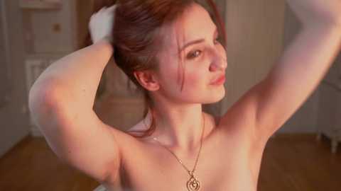 Media: Video of a fair-skinned, red-haired woman with a slender physique, adjusting her hair in a softly lit room. She has a delicate face and wears a gold necklace.